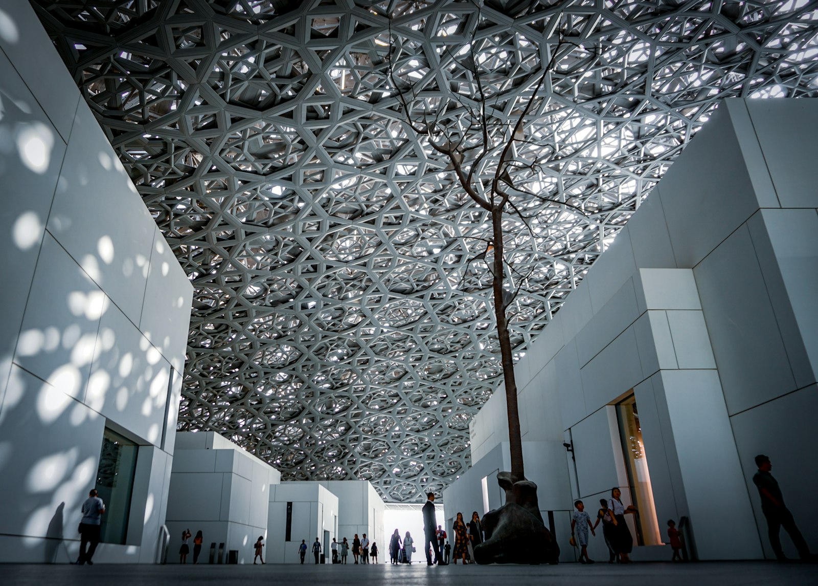 Couple walking hand in hand along the Louvre Abu Dhabi's rain of light dome with the sea in the background
