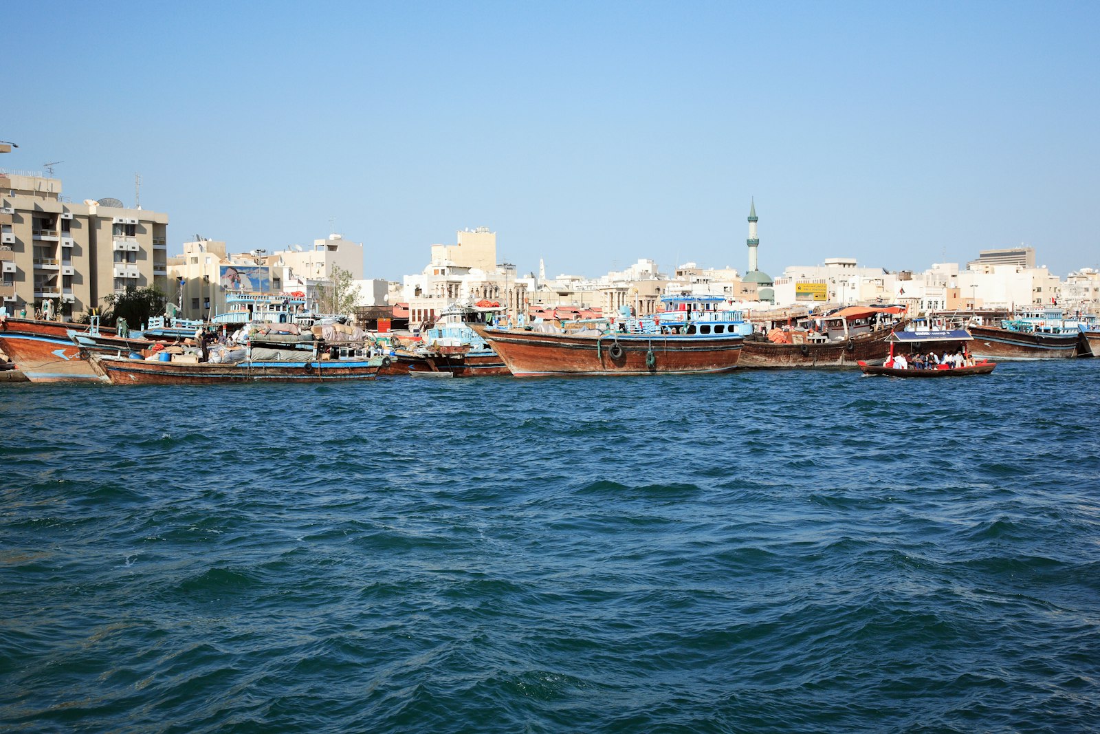 Family riding a traditional abra boat across Dubai Creek with the old souks in the background